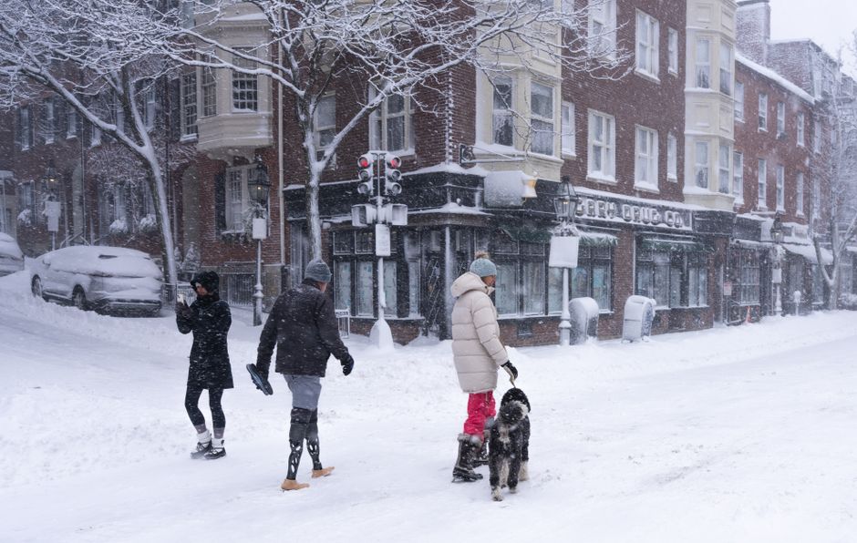 Snowy day in Boston with people and dog walking through historic streets amid snowfall.