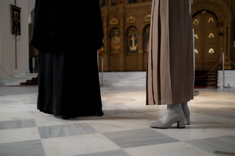 Partial view of elegantly dressed figures inside a historic church with ornate background.